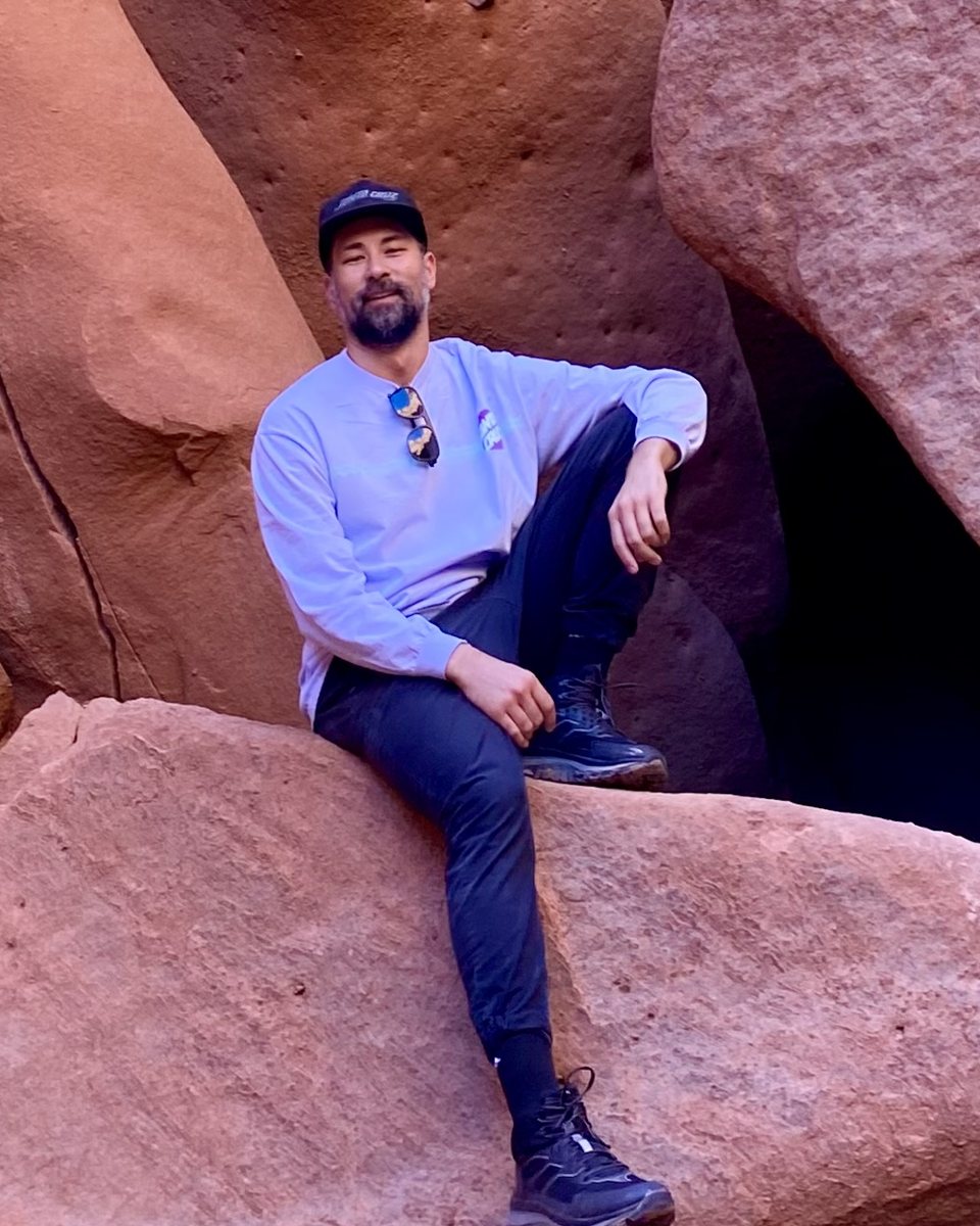 Jacob Ando smiling, seated on a boulder in a red sandstone canyon